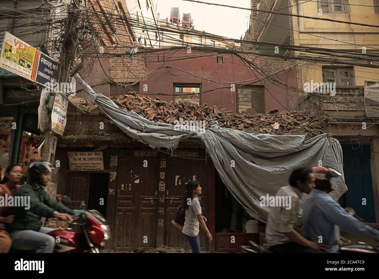 Pedestrians walking on a street in Thamel, Kathmandu, with a damaged building in the background. Stock Photo