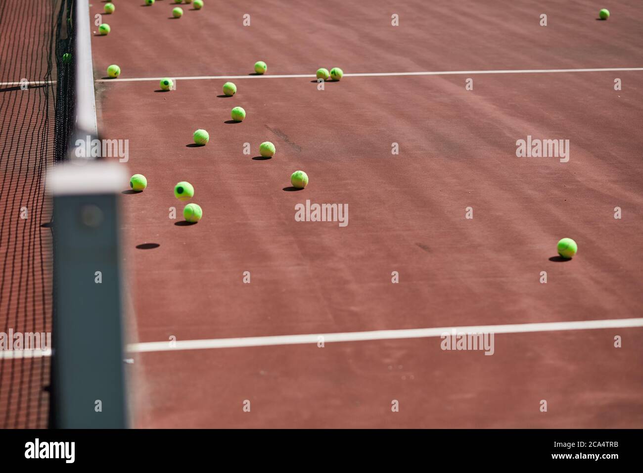Red-clay tennis court with sport equipment and tennis balls on it. Nobody is on field Stock Photo