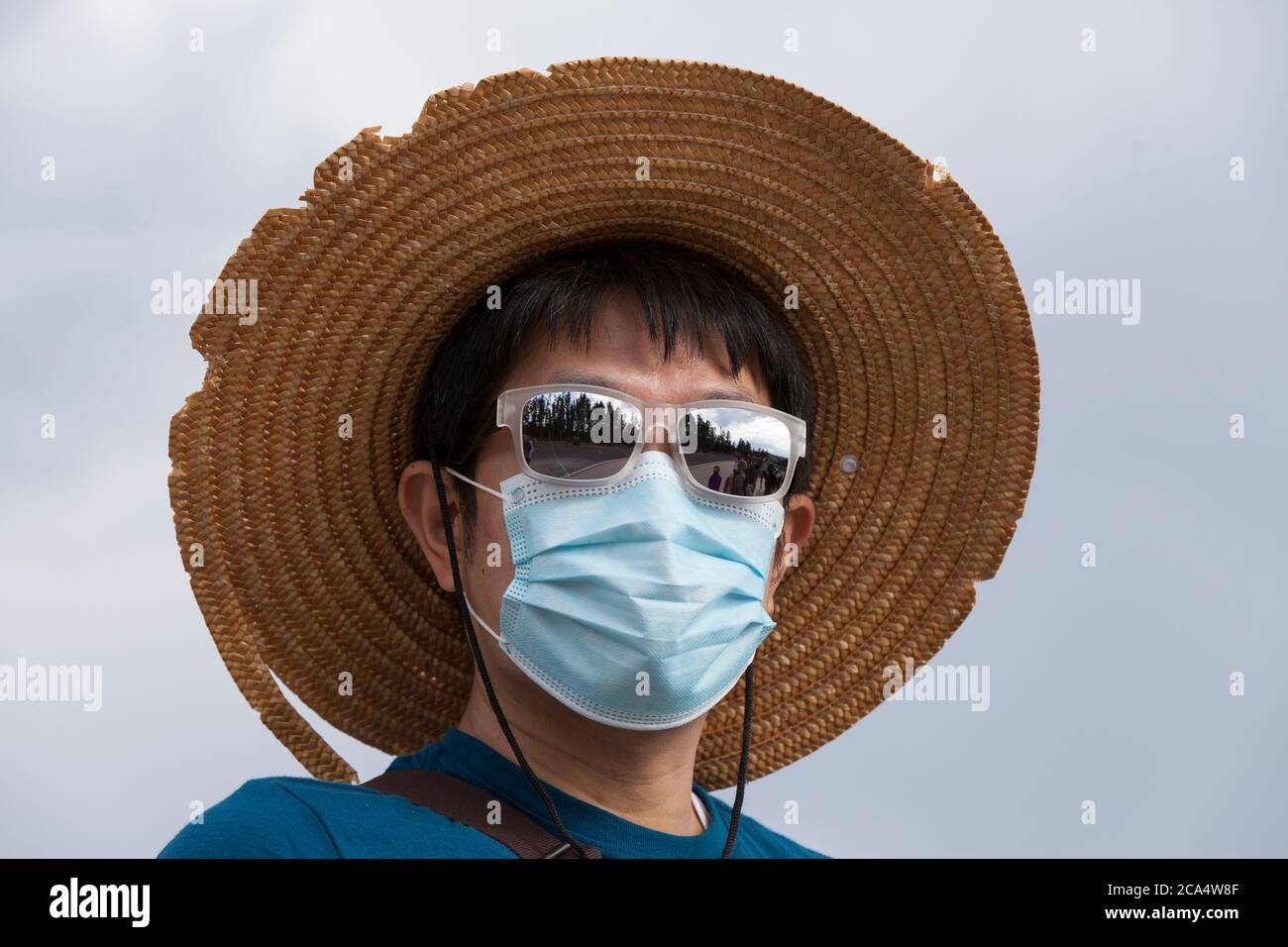 A visitor from South Korea wears a face mask while waiting for Old Faithful to erupt on Monday, August 3, 2020. The park recently reported several positive cases of the COVID-19 virus among visitors and concessioners. Stock Photo