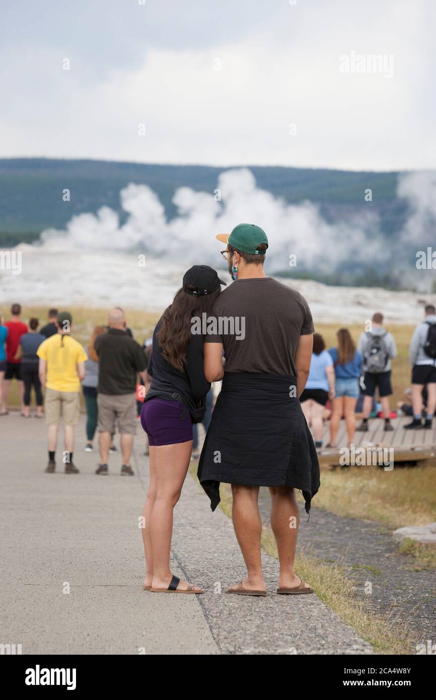 A young couple keeps their distance from the crowd while waiting for Old Faithful to erupt on Monday, August 3, 2020. The park recently reported several positive cases of the COVID-19 virus among visitors and concessioners. Stock Photo