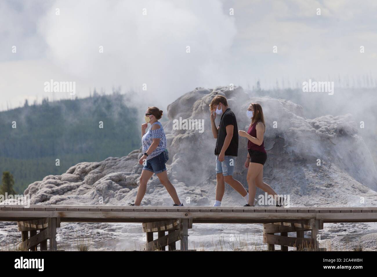 Visitors wearing face masks pass the Castle Geyser on Monday, August 3, 2020. The park recently reported several positive cases of the COVID-19 virus among visitors and concessioners. Stock Photo