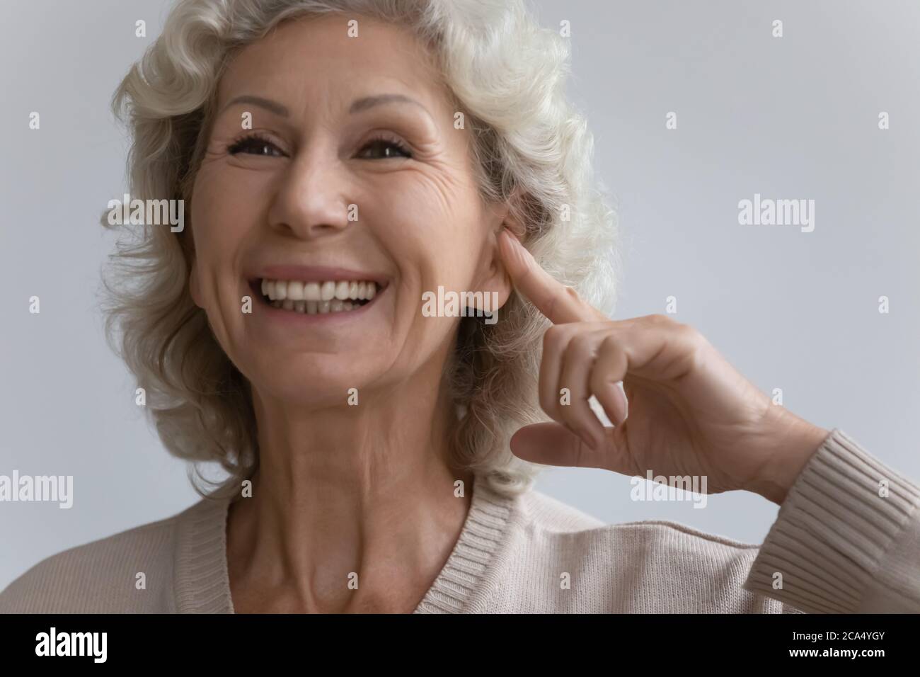 Elderly woman points finger to ear with hearing aid device Stock Photo