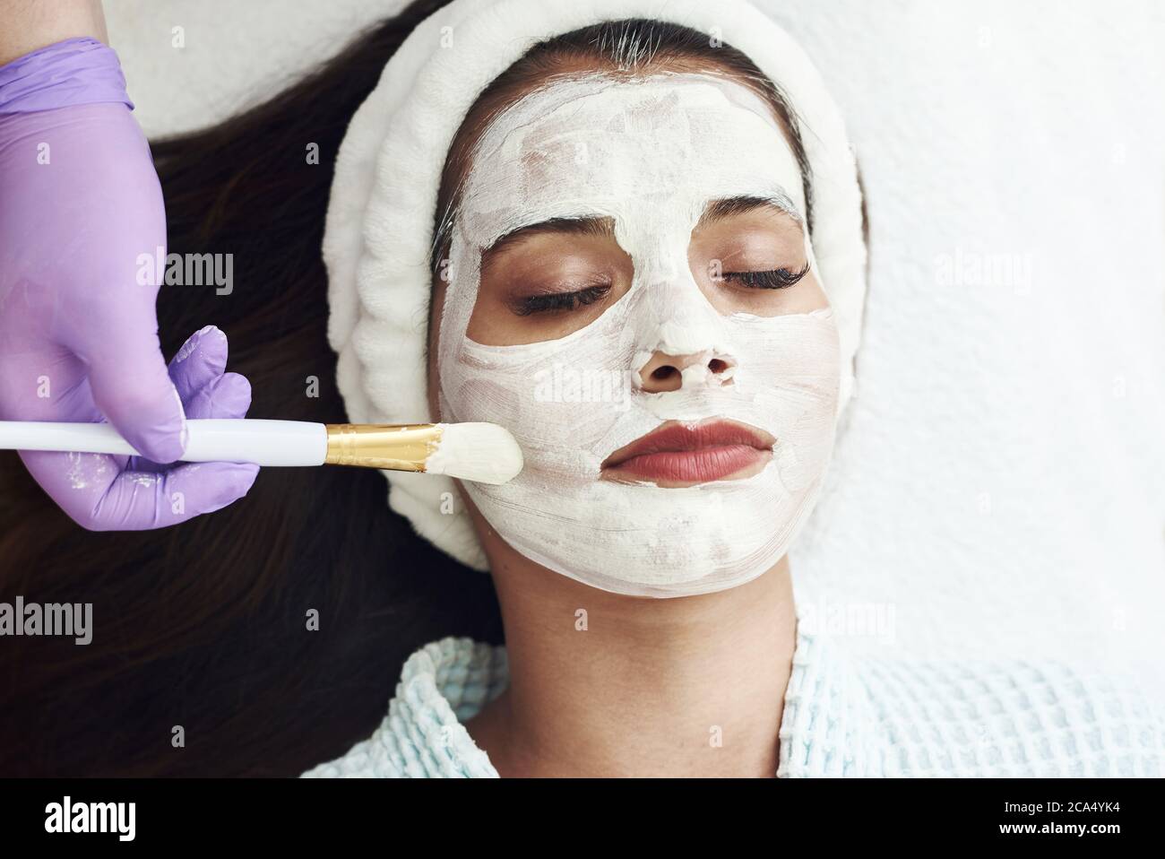 Spa concept. Young woman with nutrient facial mask in beauty salon, close up. The beautician applies a moisturizing mask to the client's face. Stock Photo