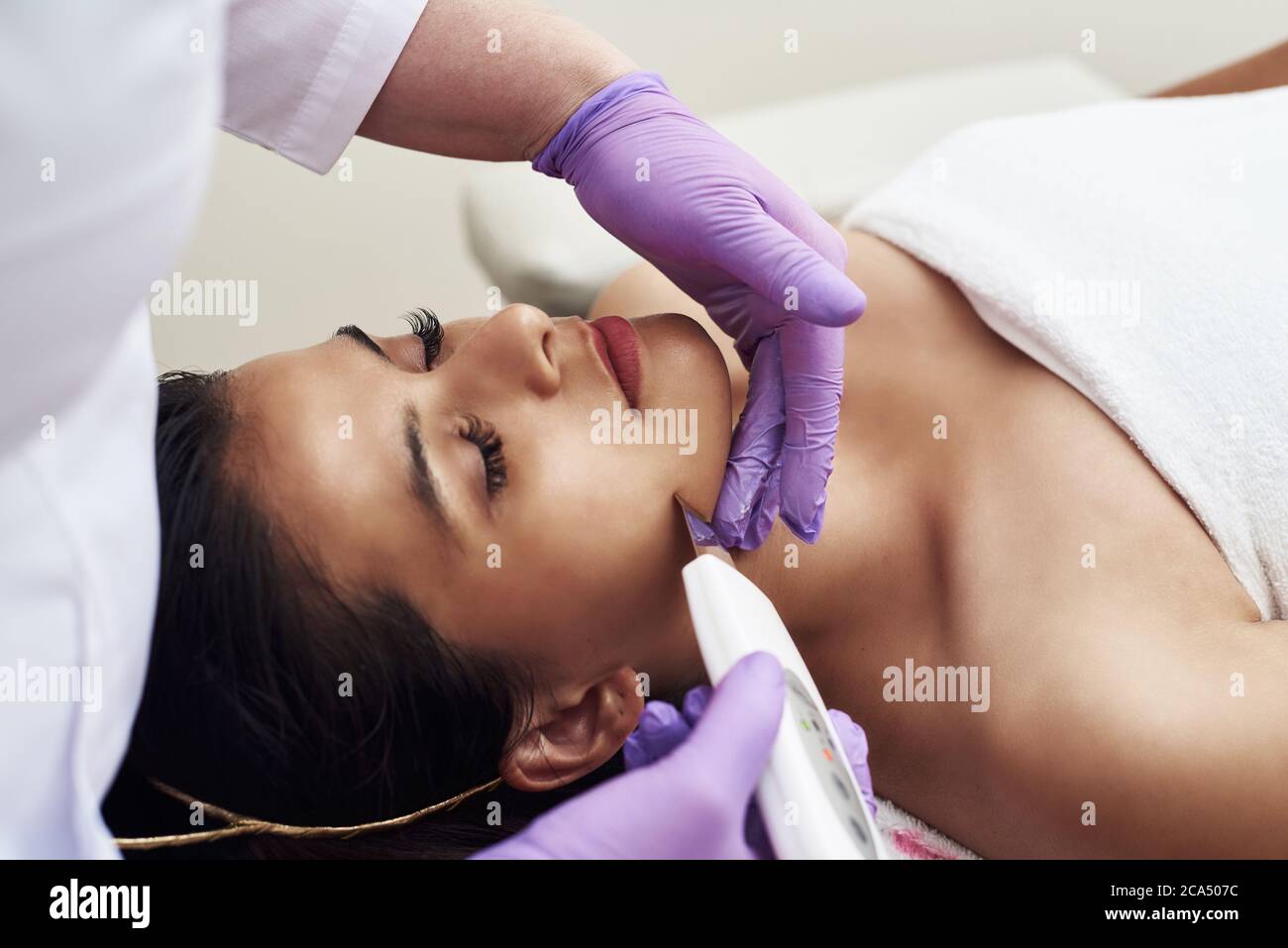 A woman makes an ultrasonic cleaning of the face and skin to a client. Modern equipment. Young pretty woman receiving treatments in beauty salons and lying on the couch. Stock Photo