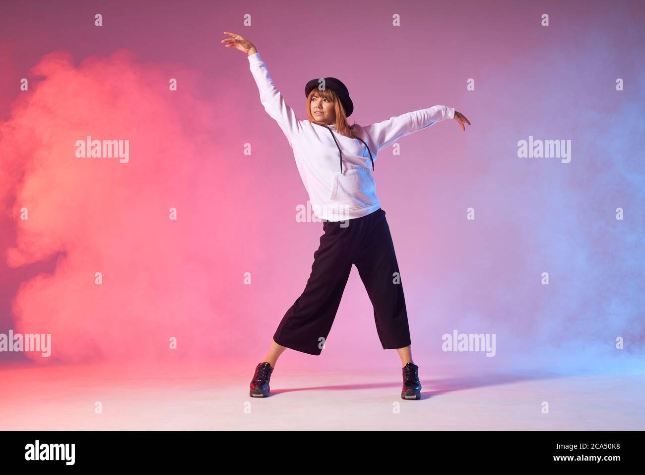 Funk dance workout. Portrait of young sporty woman in motion performing dance element, raising hands up, looking away, training in school dancehall, s Stock Photo