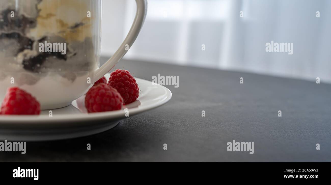 One Raspberry On A Table Cup, plate and raspberries on dark stone table for break concept in ...