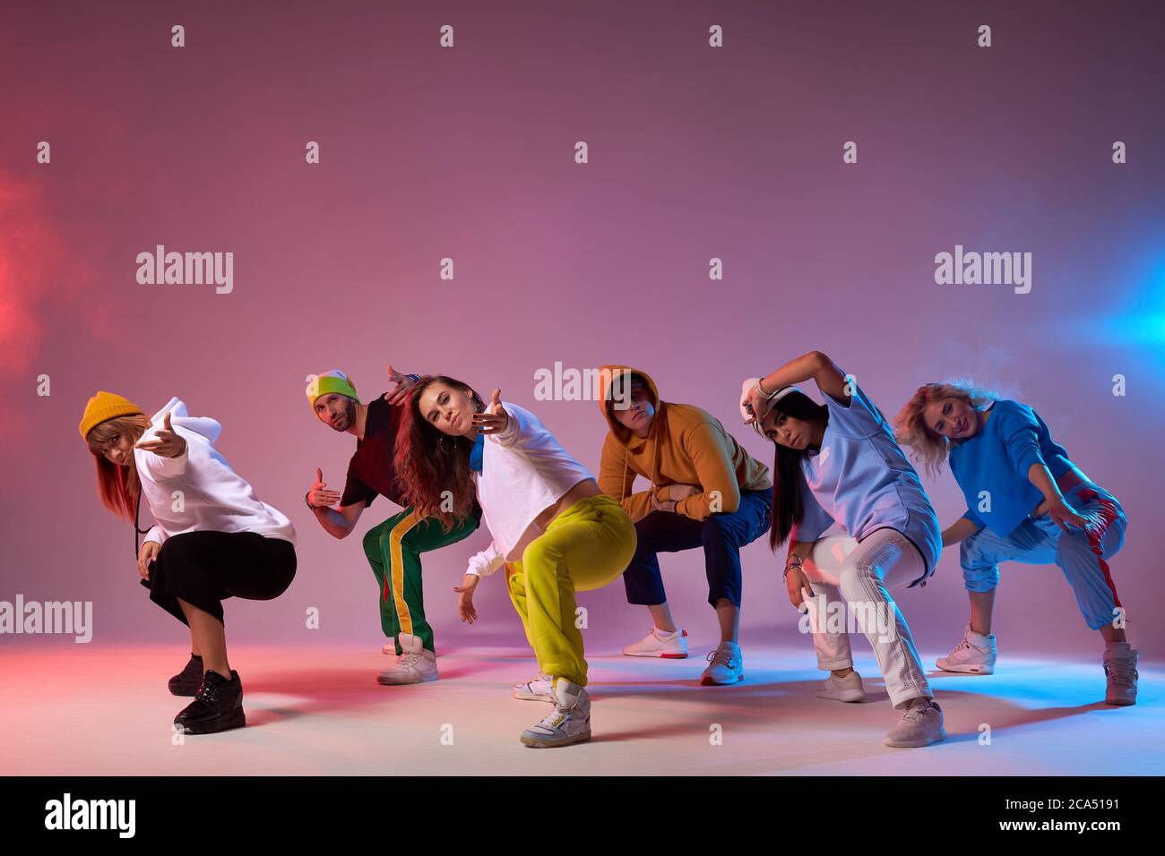 Famous group finish dancing , sitting on squats, looking at audience, making come alone gesture, expressing cheerfulness, dressed in sportswear, hip h Stock Photo