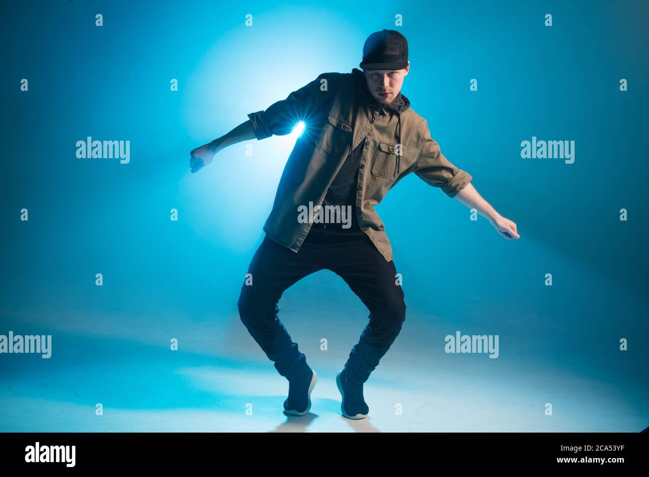 Full length portrait of a young man dancer in casual street wear dancing funky hip hop on isolated studio neon blue background Stock Photo