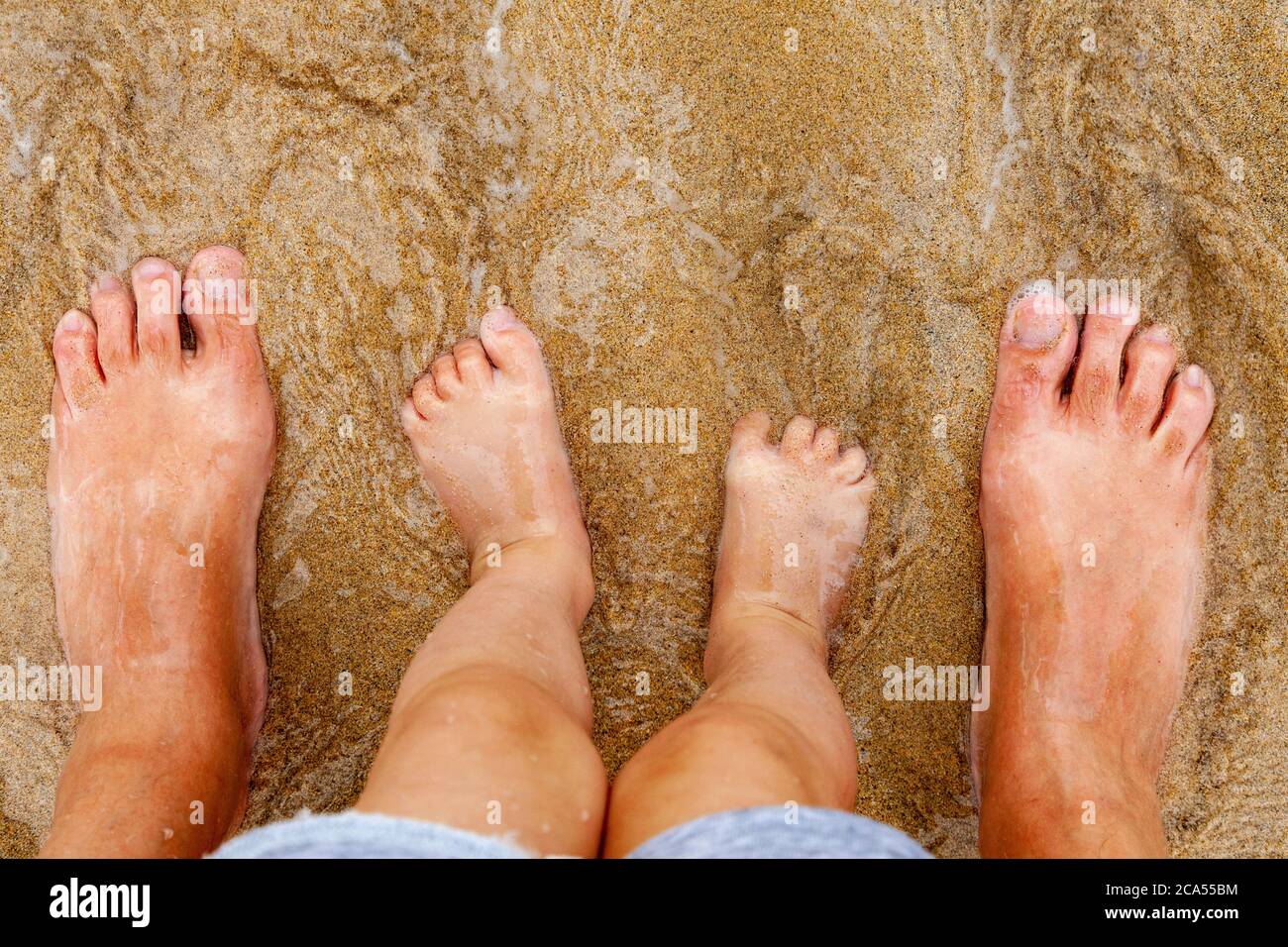 Father and daughter's feet on sand as the tide goes in and out Stock Photo