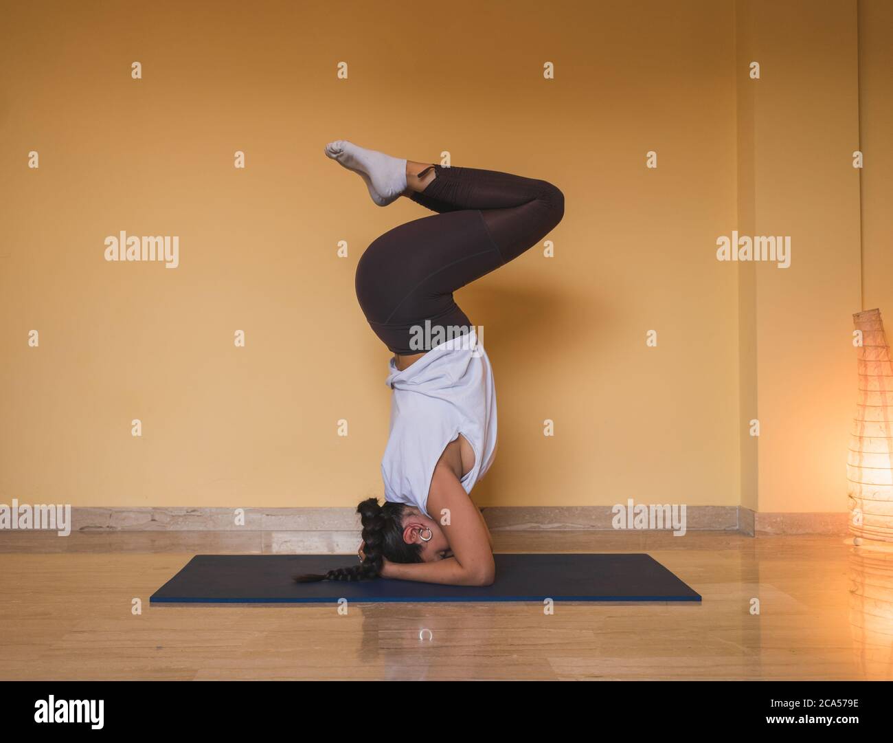 A shot of an anonymous woman starting supported headstand pose. Side view of slim female doing yoga in cozy living room during daytime at home. Stock Photo
