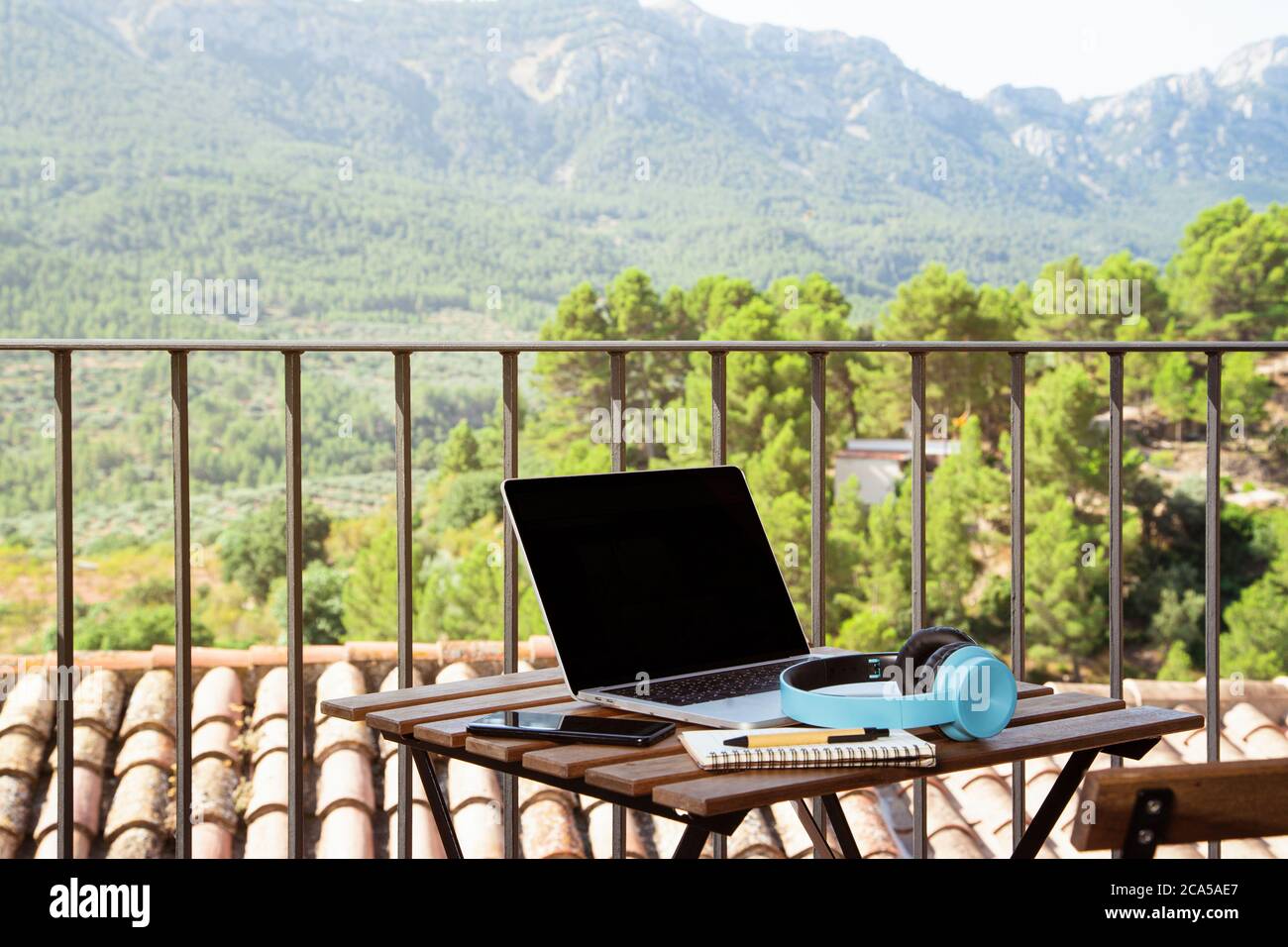 Still life view of open laptop computer on a wooden patio patio table with mobile headphones and notepad in outdoor home area, outdoors. Technology at Stock Photo