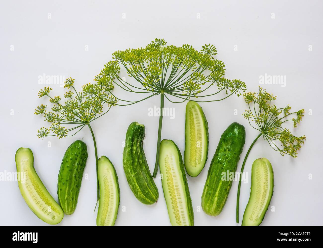 Halved cucumbers and fresh dill on a white surface. Stock Photo