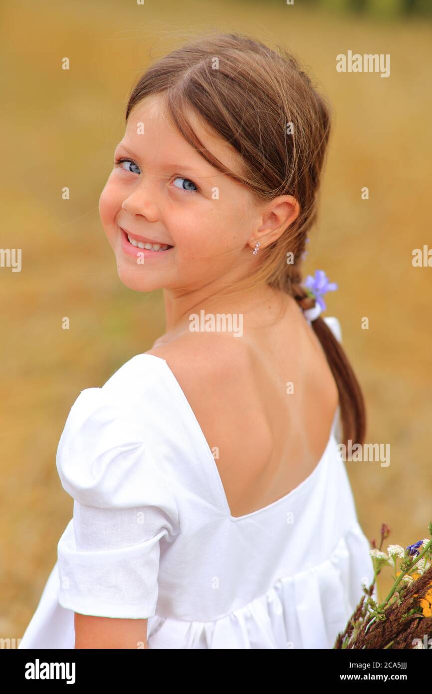 Little girl with a bouquet of wildflowers in her hands in a wheat field ...