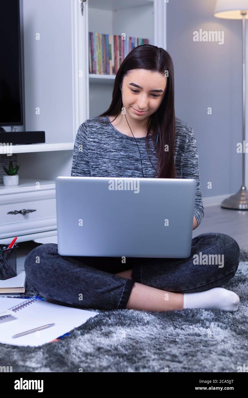 Student girl with laptop and headphones studying online at home. Education or leisure concept. Focus on her. Stock Photo