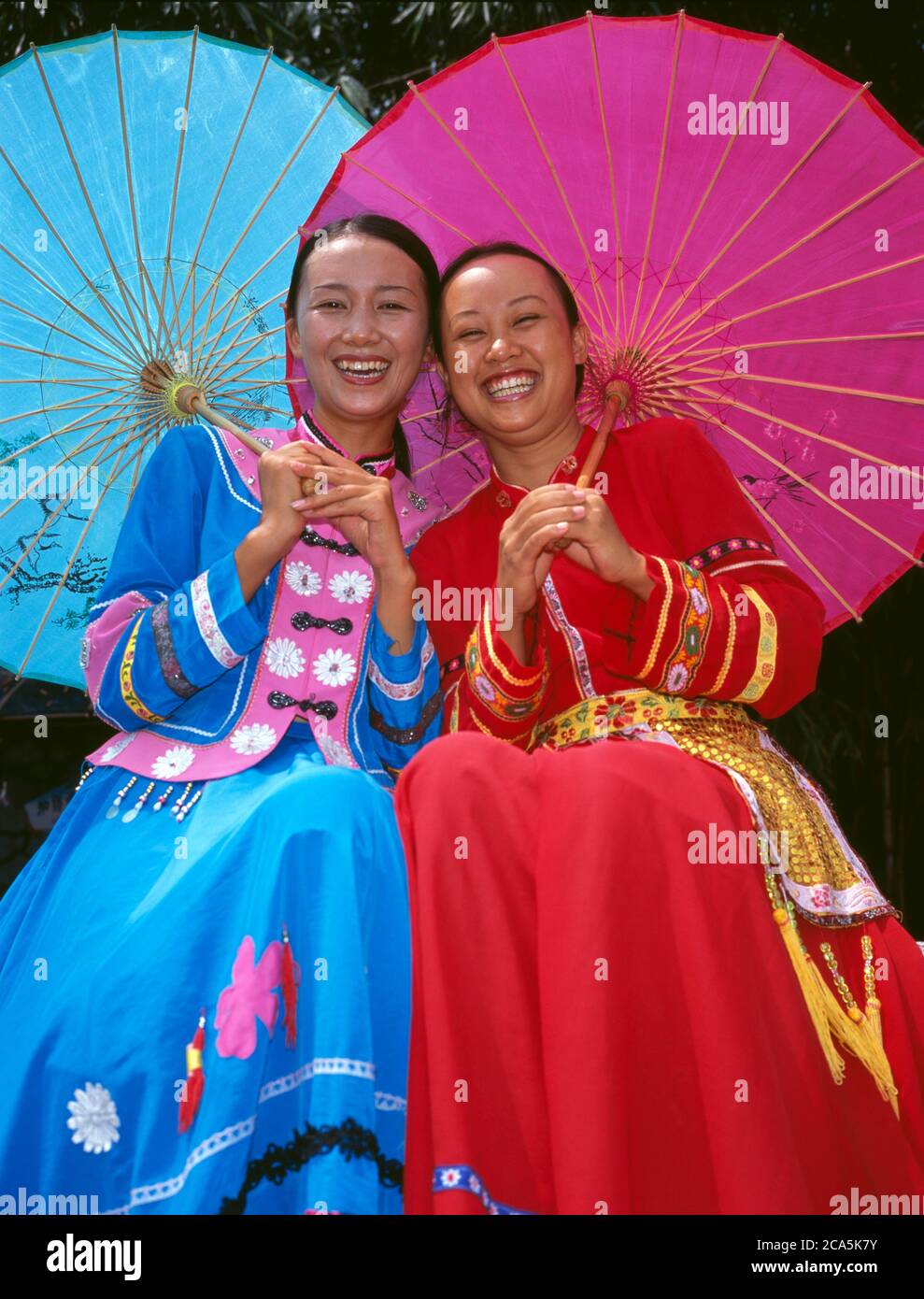 Two Smiling Young woman wearing traditional Chinese clothing, holding Umberella in a park, Yunnan, China Stock Photo