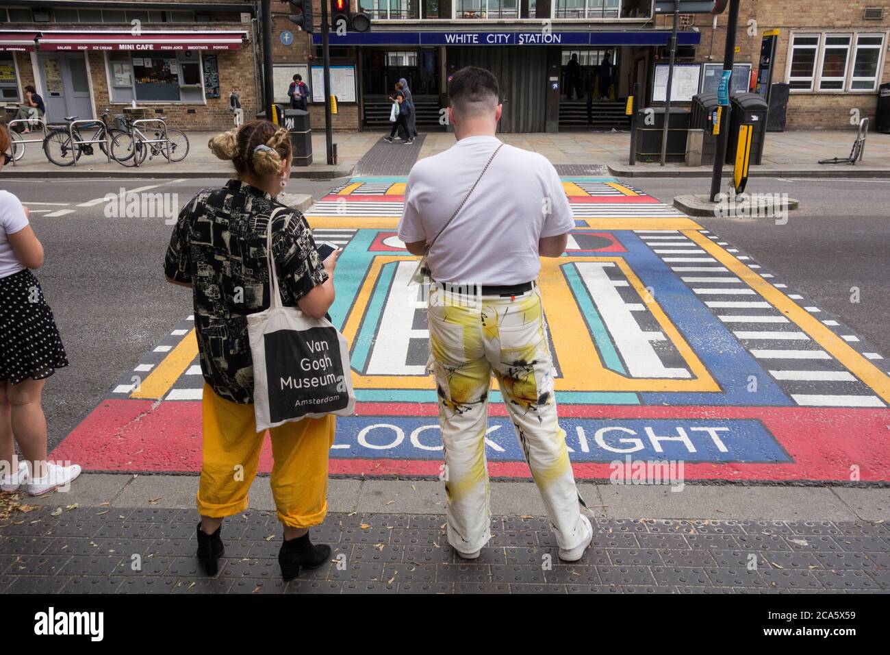 A couple waiting next to French artist Camille Walala's geometric pedestrian crossings outside White City underground station in west London, UK Stock Photo