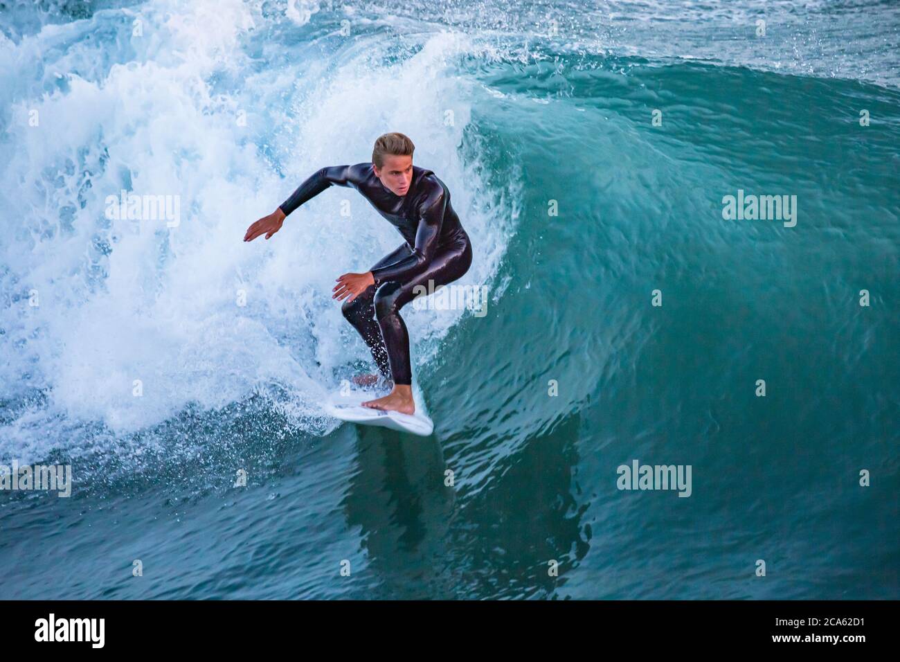 Attractive young male surfer riding a wave at Huntington Beach, CA Stock Photo