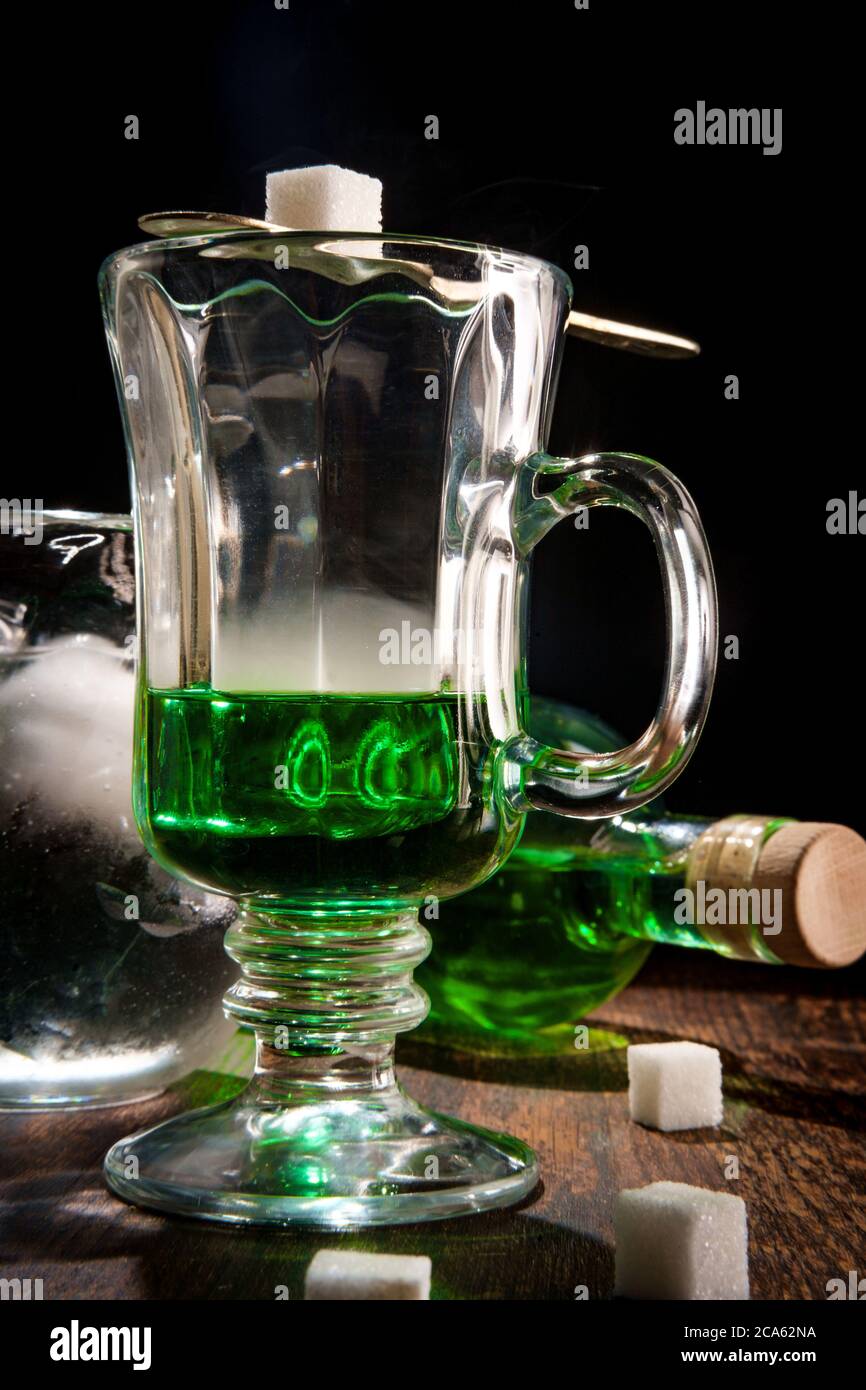 Green absinthe liquor in glass with ice water to pour over sugar cube