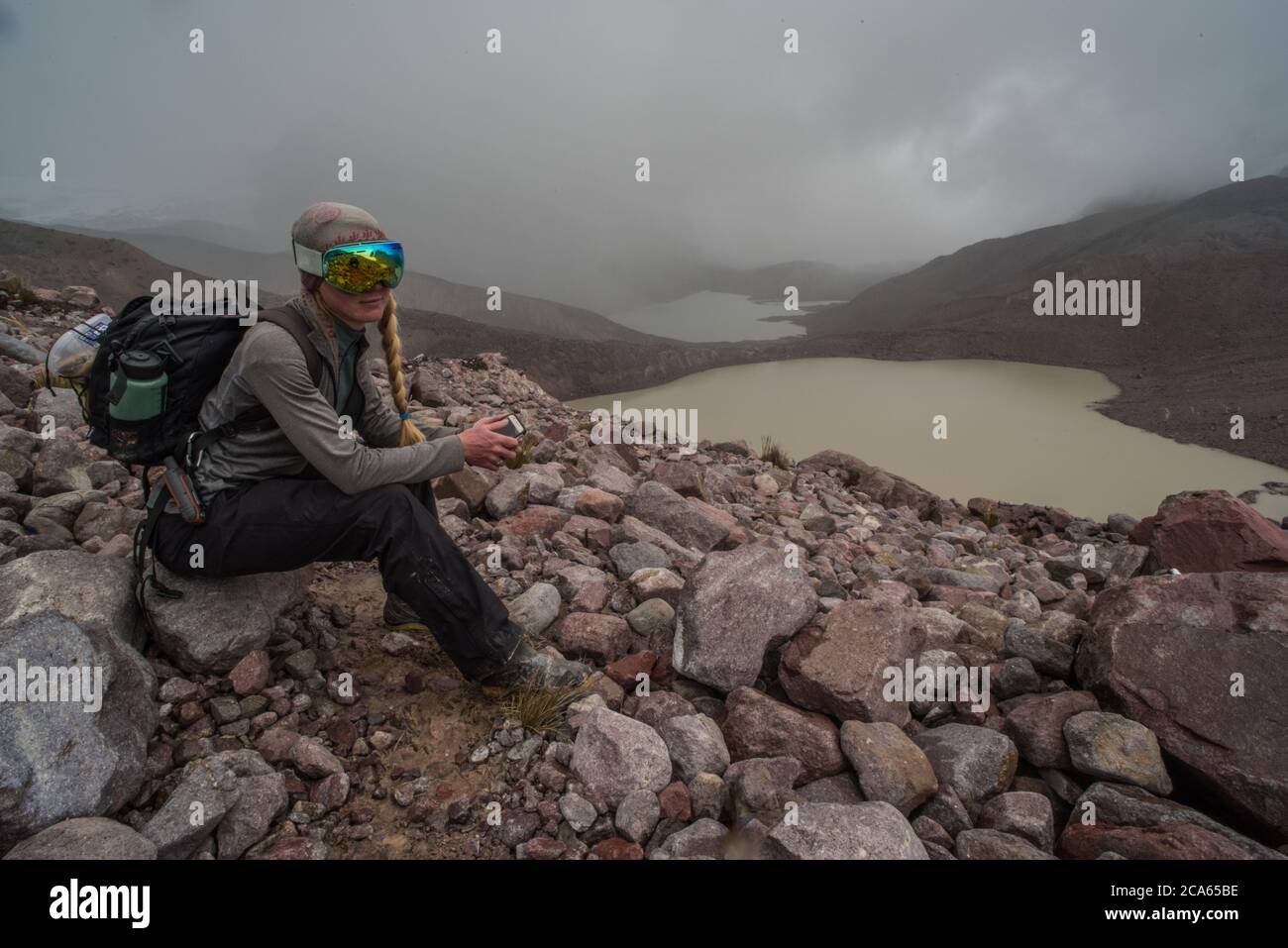 A biologist hiking through the Cordillera Vilcanota takes a break and sits on a stone high in the Andes mountains where there is little oxygen. Stock Photo