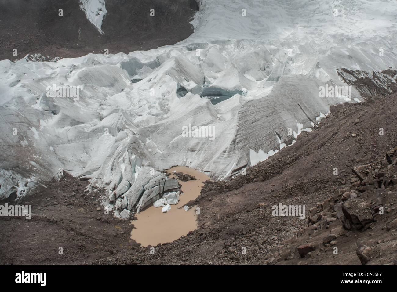 A large tropical glacier high in the Peruvian Andes slowly recedes and melts, melt water flows away from it.  It may not last more than a few decades. Stock Photo