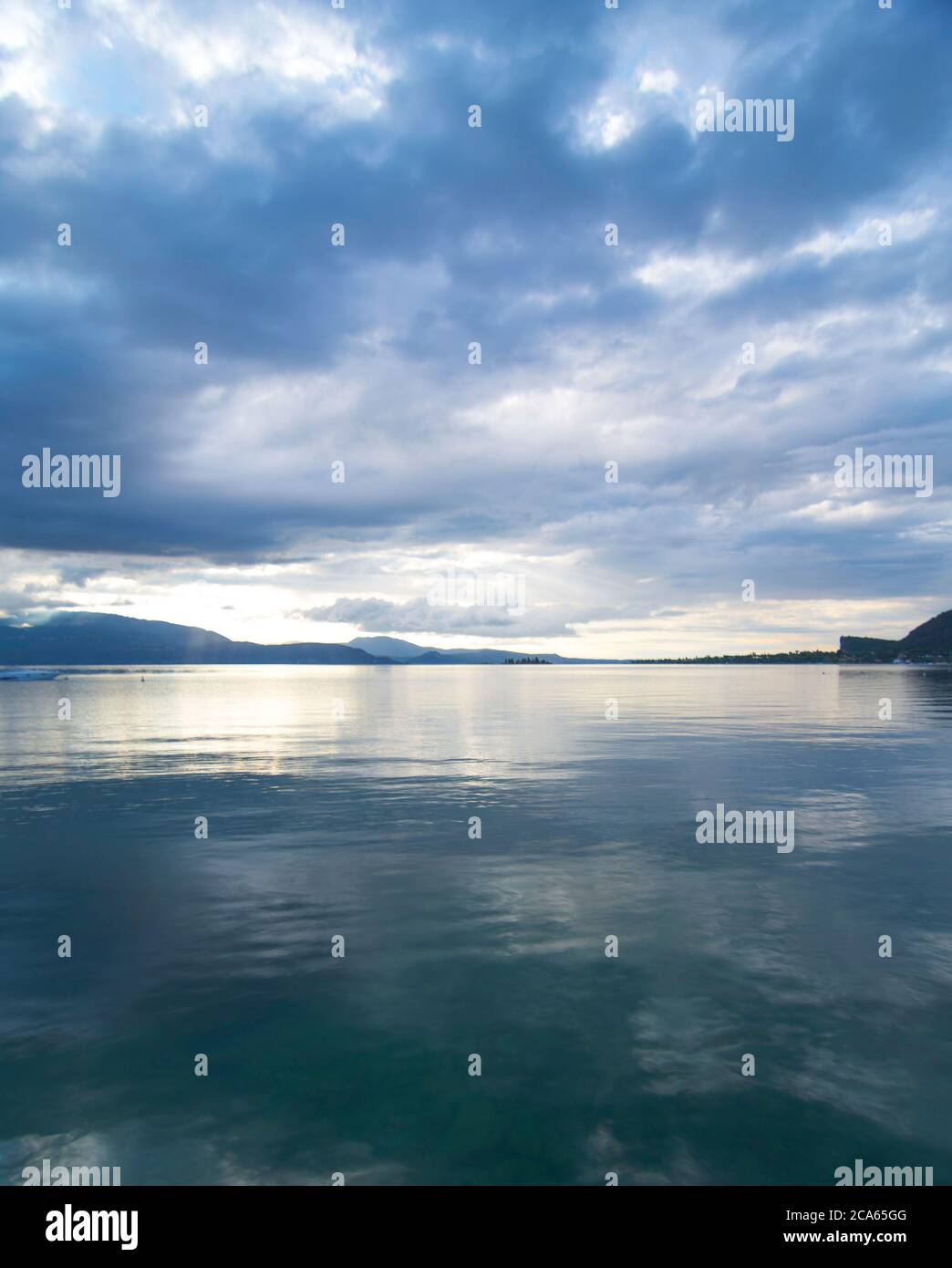View of Lake Garda in the early morning or evening. The water is calm, the sky is partly cloudy. Small boats dance on the water. The mood is dreamy. Stock Photo