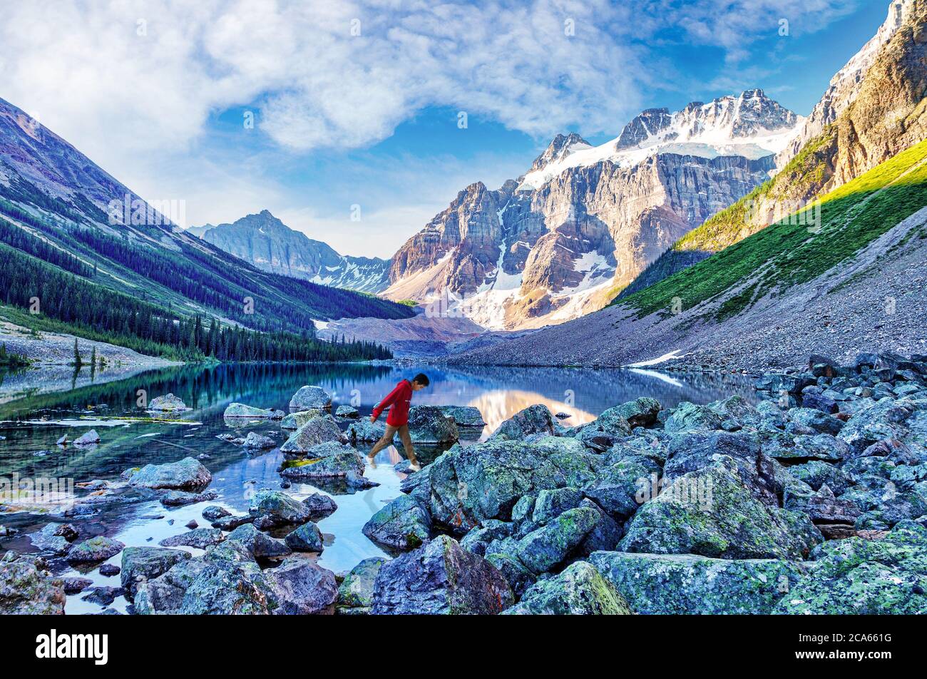 Teenage boy hiker rock hopping across Consolation Lake near Lake Louise in Banff National Park, Alberta, Canada, with Mount Quadra in the background. Stock Photo