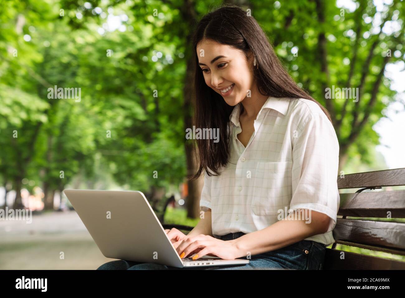 Photo of happy asian woman using laptop and wireless earphone while ...
