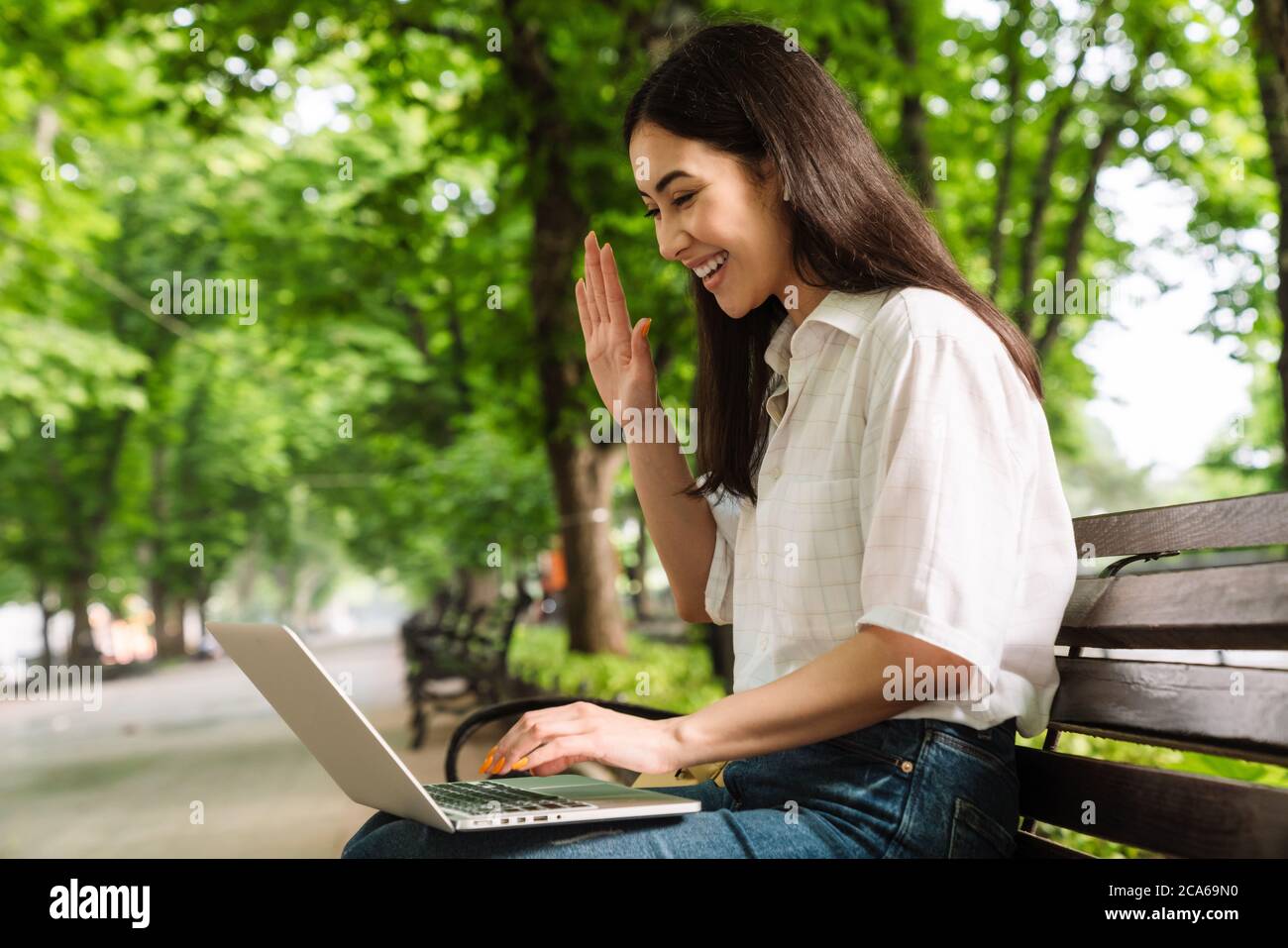 Photo of happy asian woman using laptop and waving hand while sitting ...
