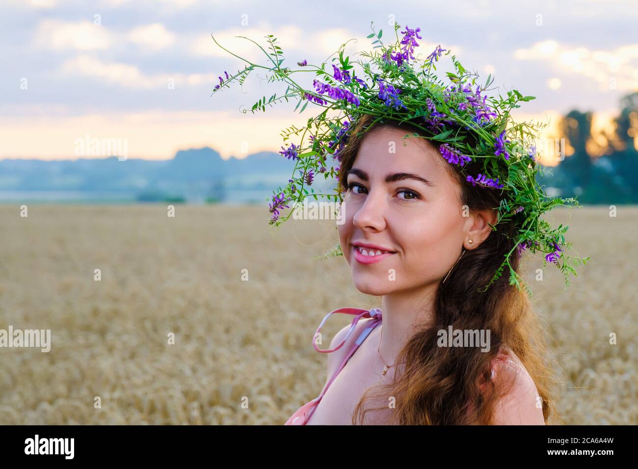 Happy smiling girl with long hair with a flower wreath on head in wheat ...