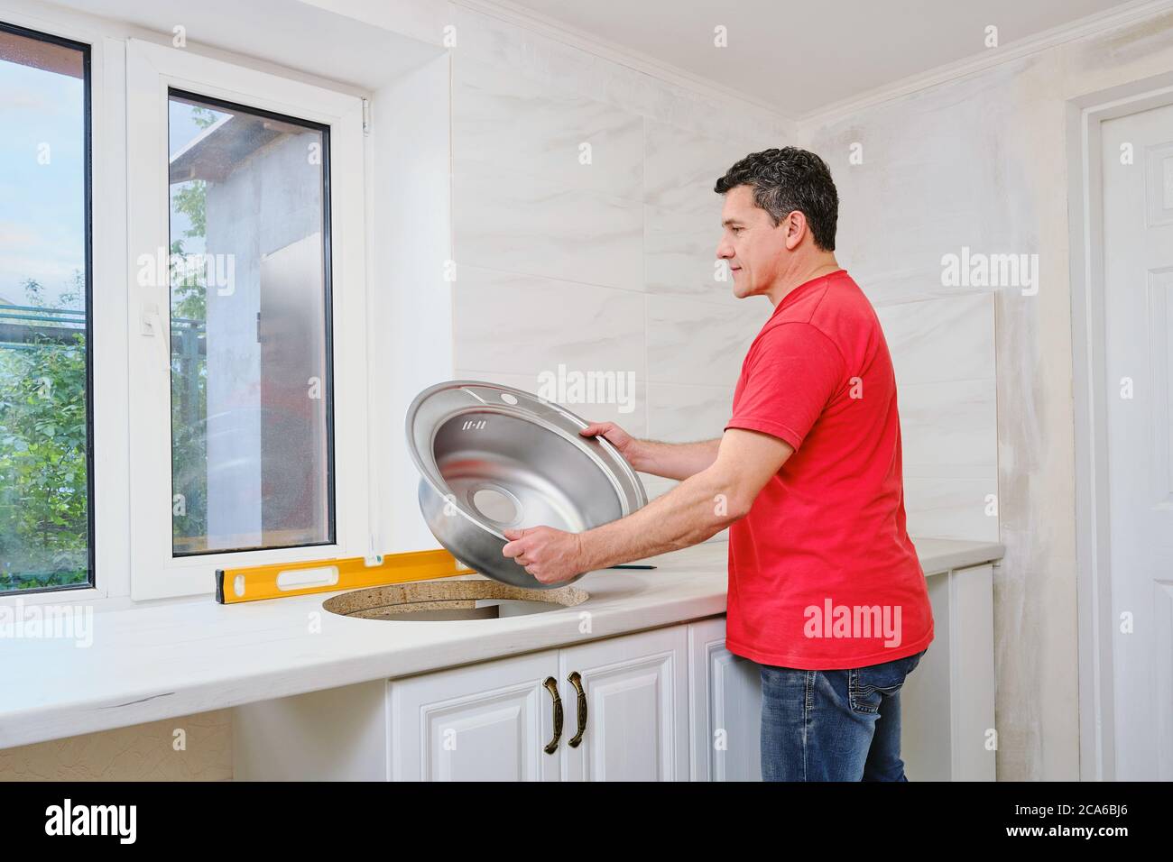 white man installs round single stainless steel sink into a cut-out hole  Stock Photo