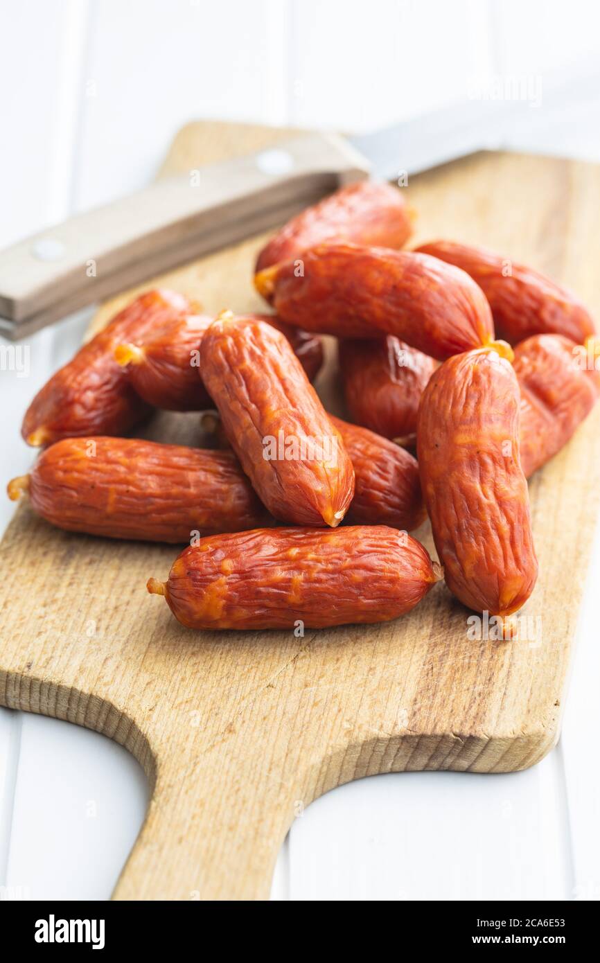 Mini salami sausages on wooden cutting board on white table Stock Photo