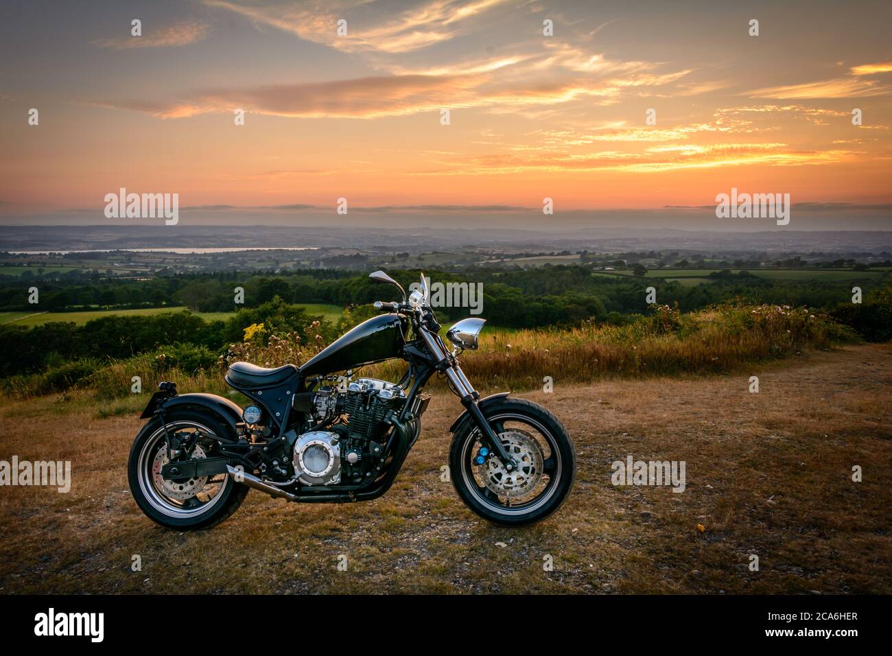 A custom made motorcycle (chopper) parked up on a quiet summer evening with the River Exe estuary in Devon in the background Stock Photo