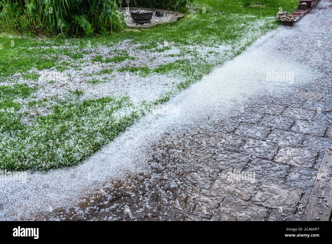 View at stone path and green garden with hail stones during hailstorm from sky with sunlight Stock Photo