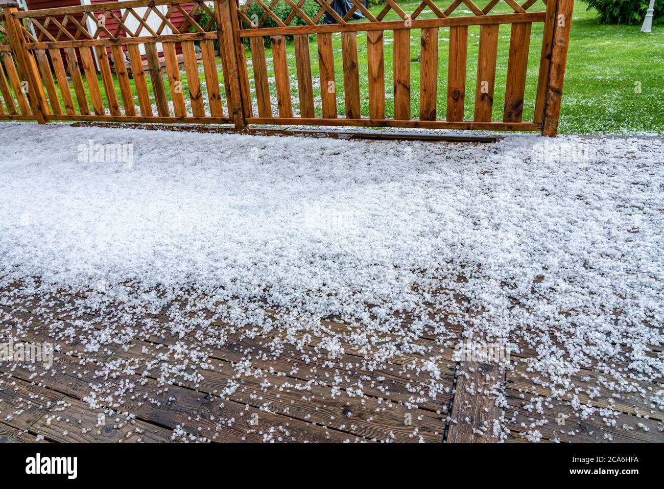 View at wooden terrace with hail stones during hailstorm from sky with sunlight Stock Photo