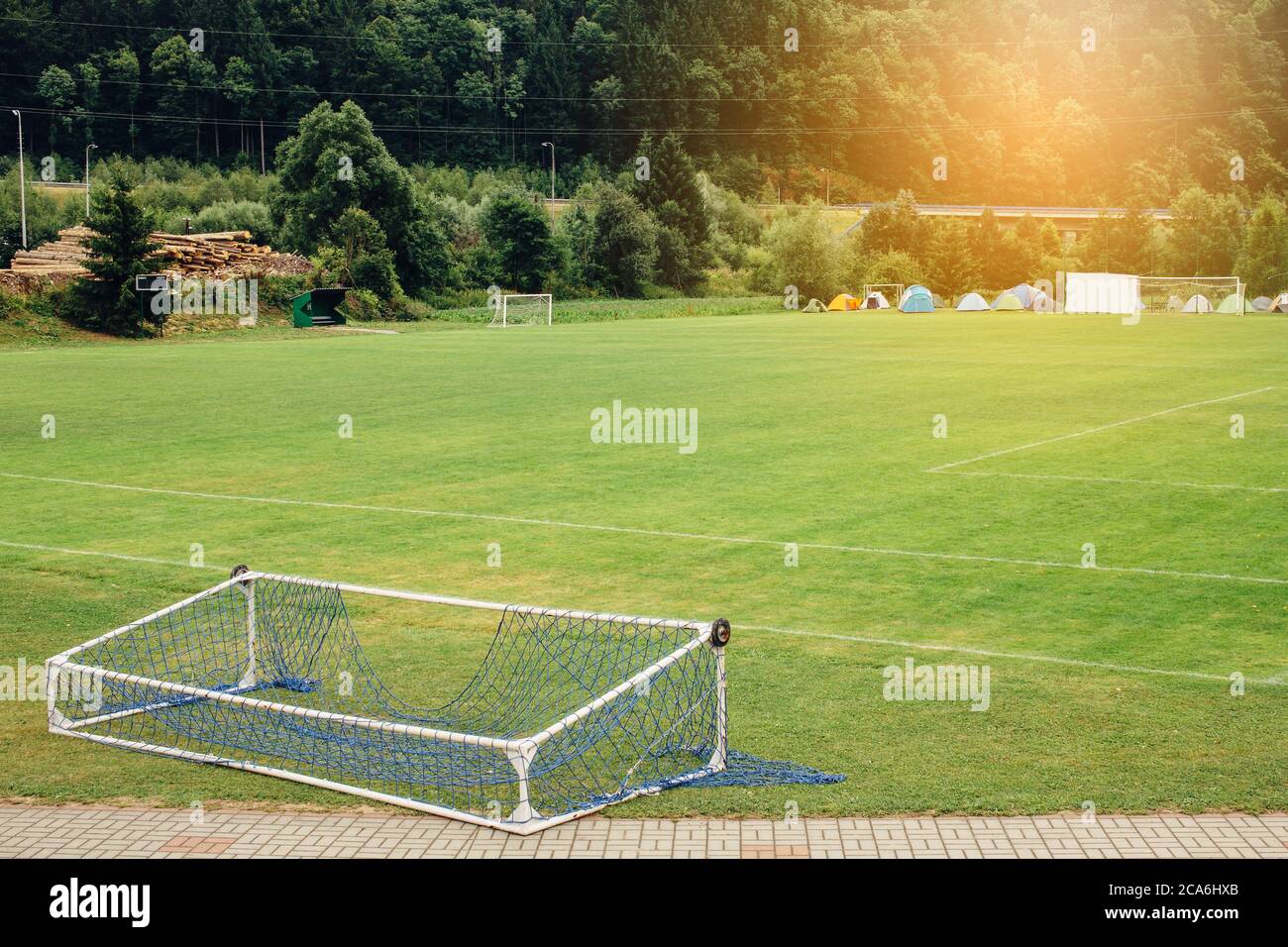 Fallen soccer football gate lying on empty green field with camping tents in the background Stock Photo
