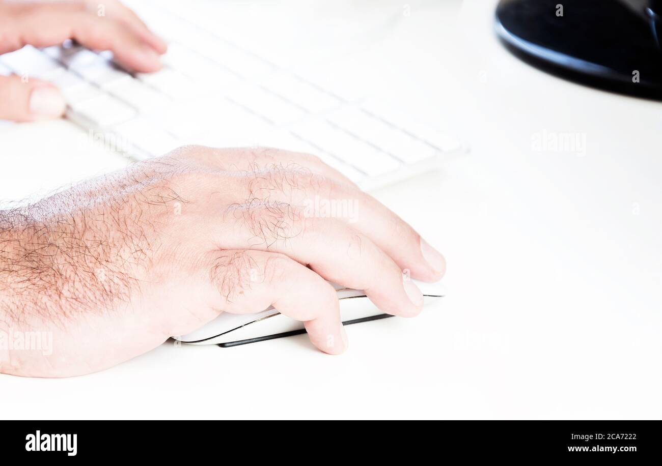 male hand clicking on a white mouse with a white keyboard on the right. White table in a office. Technology and business Stock Photo