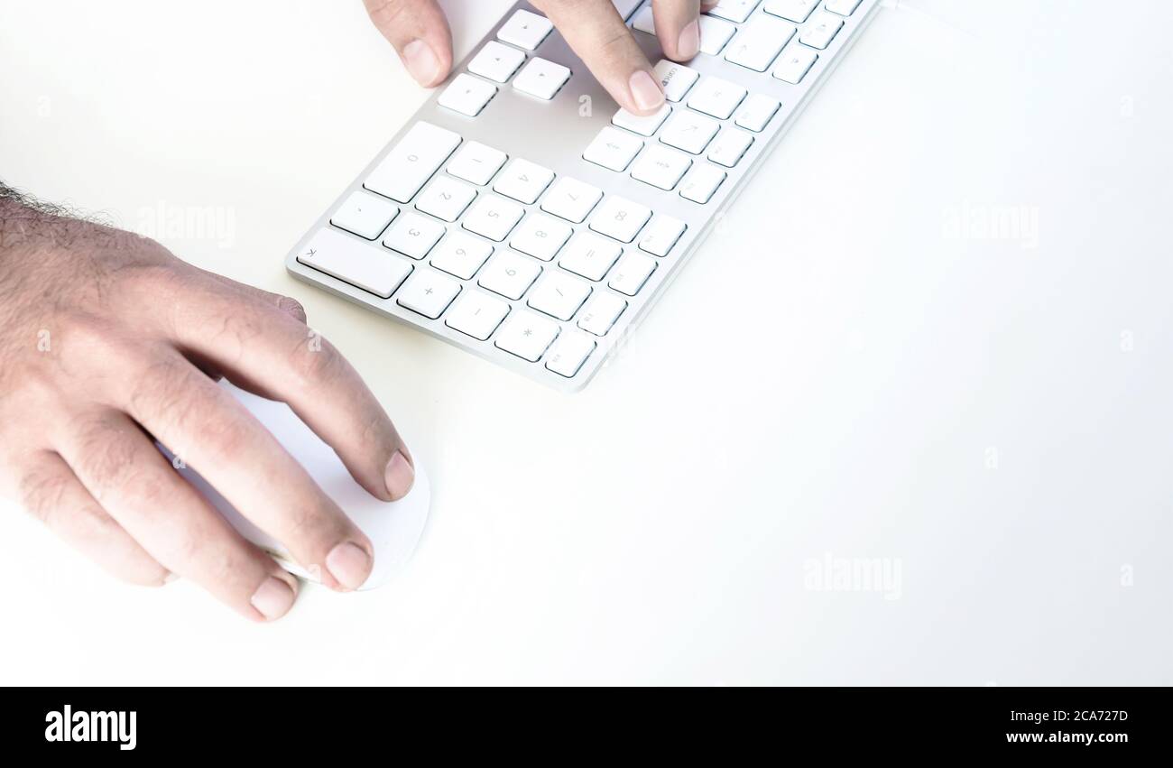 male hand clicking on a mouse and typing on a white keyboard on a white table. White background. Stock Photo