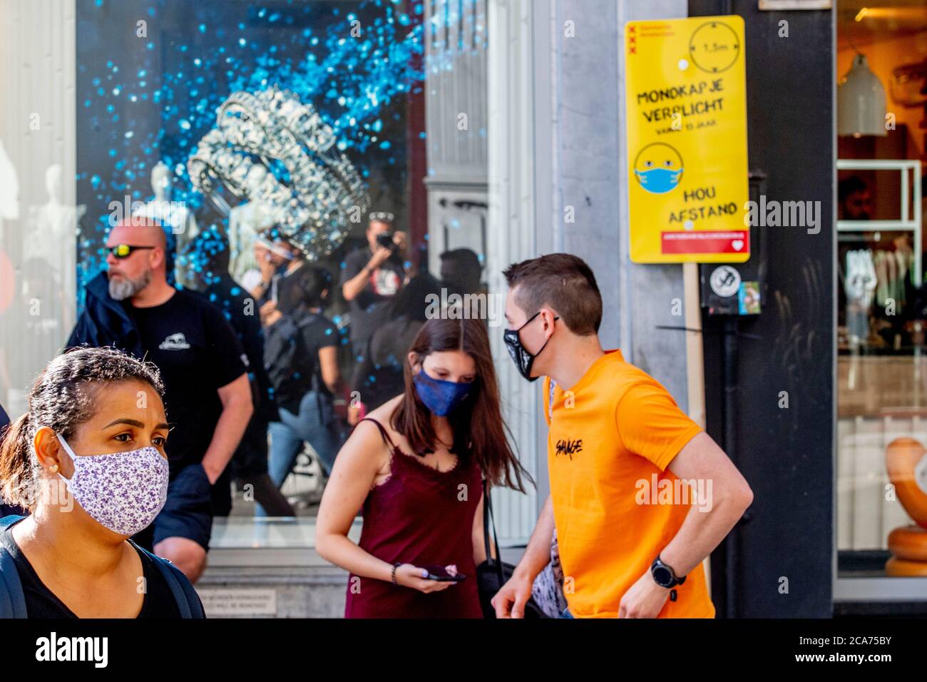 Shoppers wearing masks pass by a notice informing people about the mandatory wearing of masks on calf street. As of 5th August, wearing of face masks is going to be mandatory in busy places in Amsterdam such as malls, shopping streets, public transport and all public places following the recent concerns about a wide return of coronavirus in the Netherlands. Stock Photo