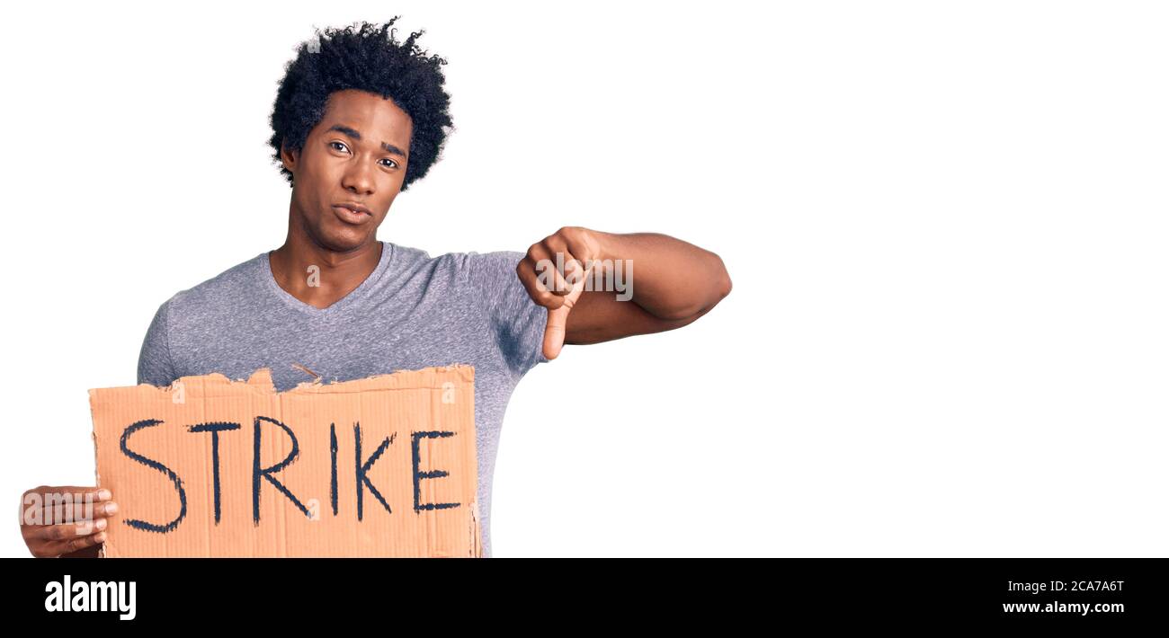 Handsome african american man with afro hair holding strike banner cardboard with angry face, negative sign showing dislike with thumbs down, rejectio Stock Photo