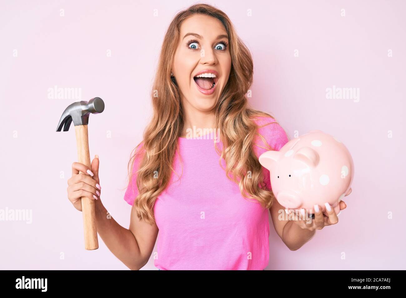 Young caucasian woman with blond hair holding piggy bank and hammer ...