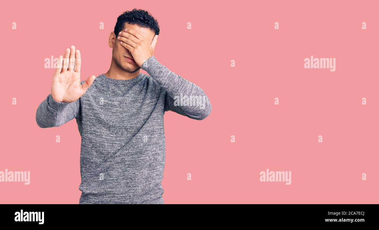 Hispanic handsome young man wearing casual sweater covering eyes with hands and doing stop gesture with sad and fear expression. embarrassed and negat Stock Photo