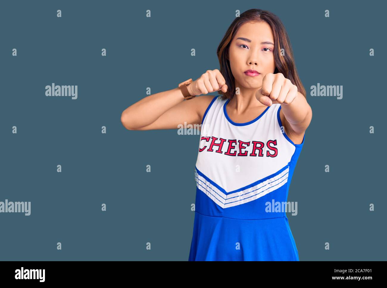 Young beautiful chinese girl wearing cheerleader uniform punching fist to fight, aggressive and angry attack, threat and violence Stock Photo