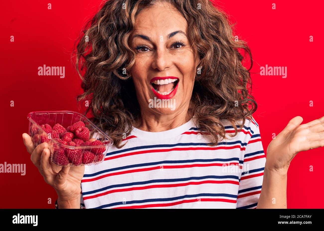 Middle age brunette woman holding box of healthy raspberries over ...