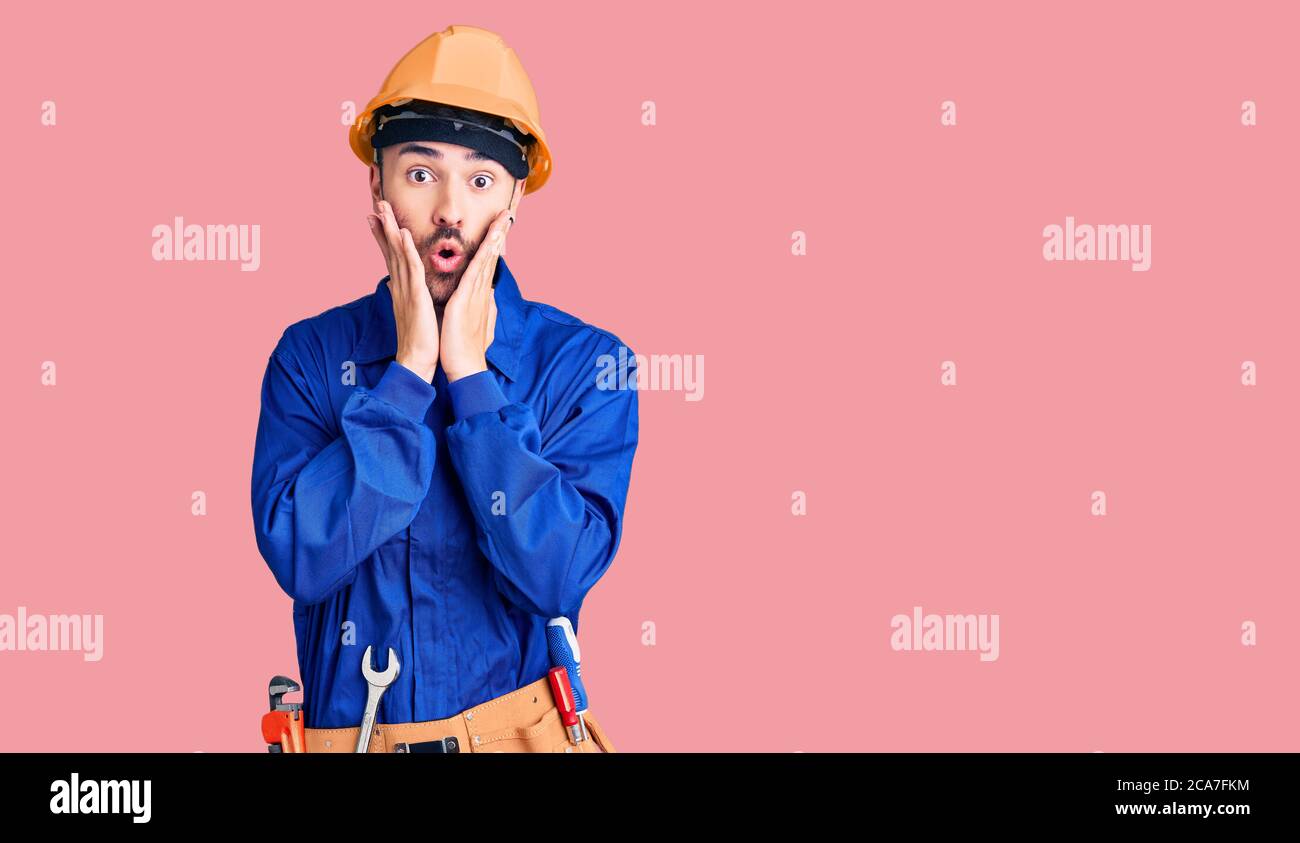 Young hispanic man wearing worker uniform afraid and shocked, surprise ...