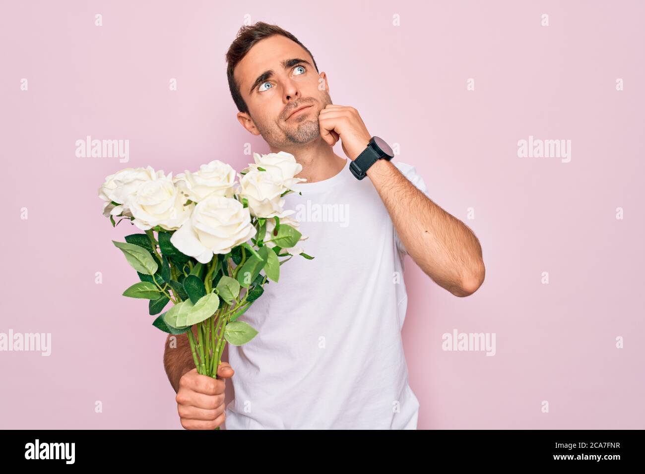 Young handsome man with blue eyes holding bouquet of flowers over pink ...