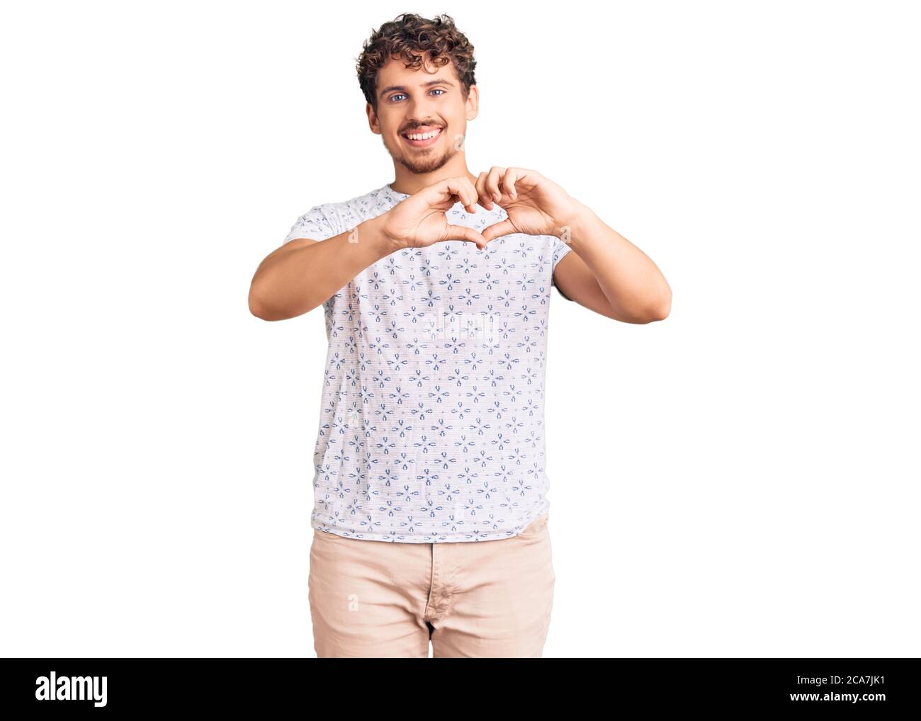 Young handsome man with curly hair wearing casual clothes smiling in love showing heart symbol and shape with hands. romantic concept. Stock Photo