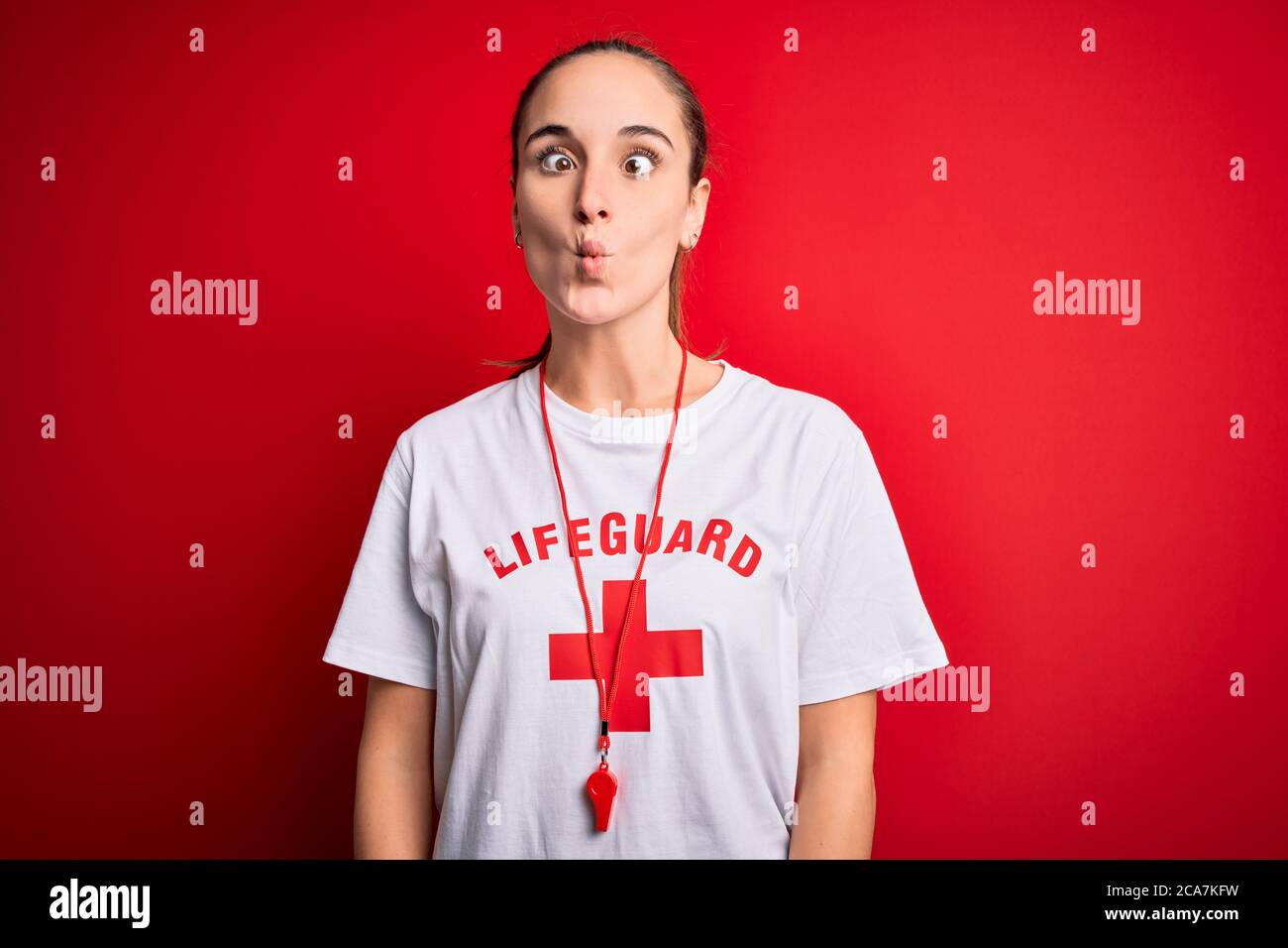 Beautiful lifeguard woman wearing tshirt with red cross using whistle