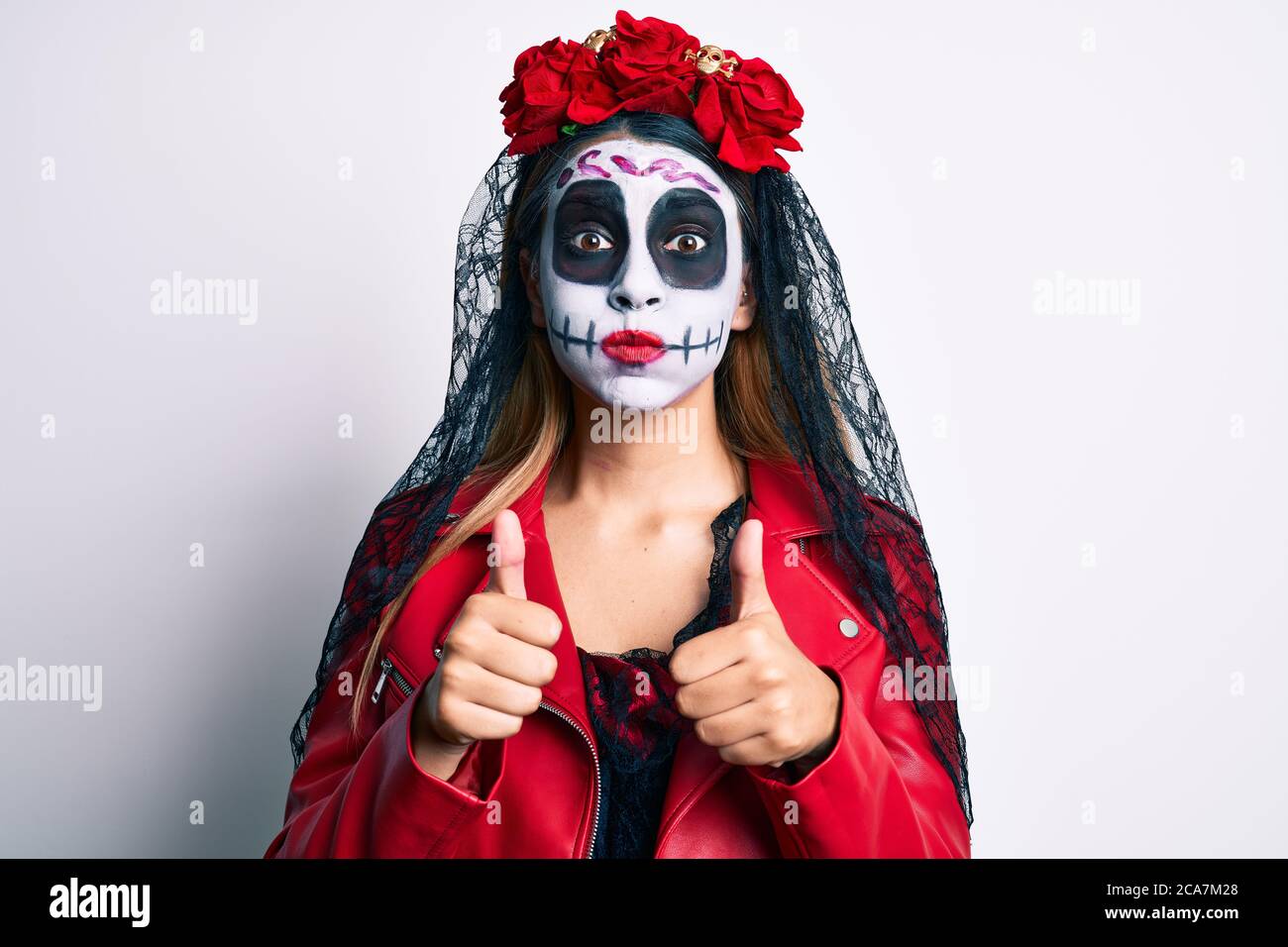 Woman wearing day of the dead costume with thumbs up doing ok sign puffing cheeks with funny face. mouth inflated with air, catching air. Stock Photo