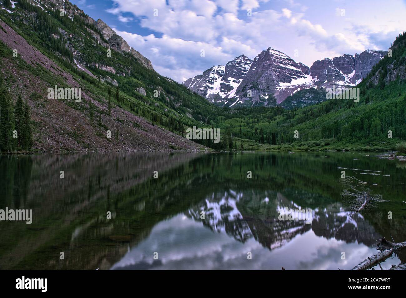 Marroon Bells at sunset. Colorful peaks reflect off glassy smooth water. Hillside leads towards the mountain showing the immense size of the snow cres Stock Photo