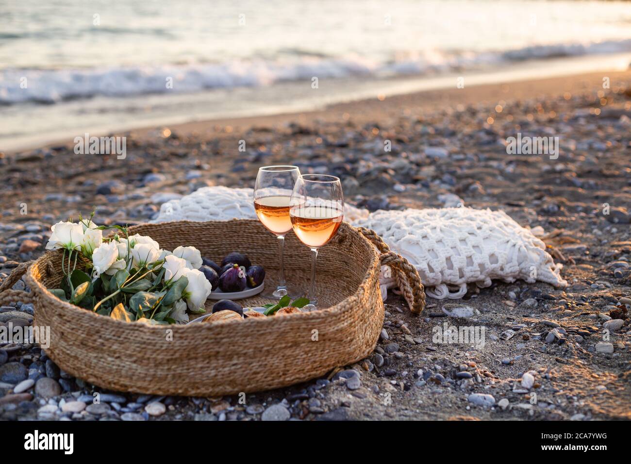 Horizontal image of the beach picnic with wine, figs, croissants and lisianthus flowers in a woven basket. Negative space. Stock Photo